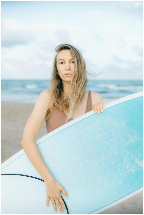 A young woman stands on a sandy beach holding a su