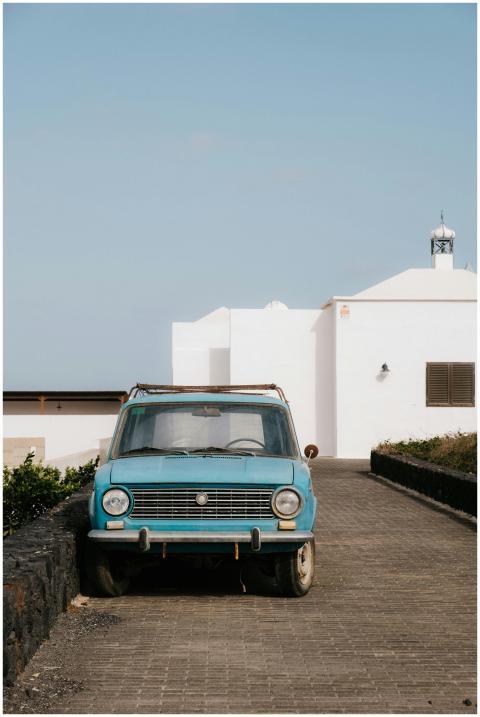 A classic blue car parked beside whitewashed build