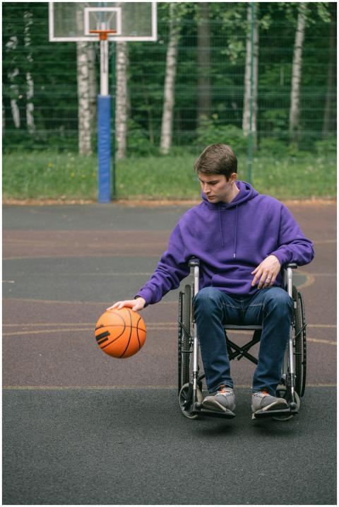 A young man in a wheelchair dribbles a basketball