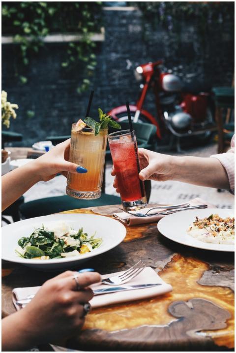 Two people clinking cocktails over a meal in an ou