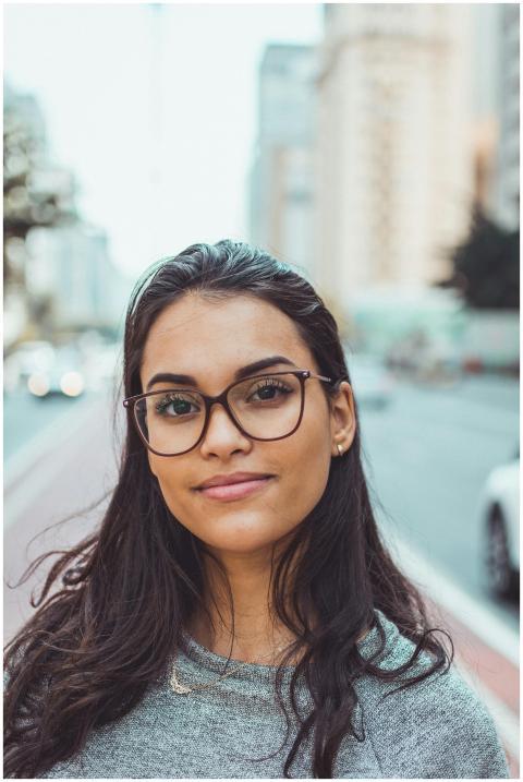 A confident woman wearing glasses smiles subtly wh