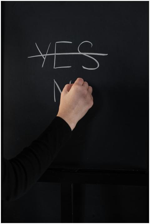 Hand writing on chalkboard with 'Yes' crossed out