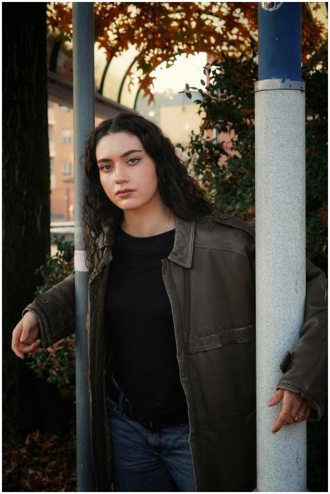 A young woman in a leather jacket leans against a
