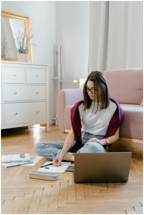 Teenager sitting on floor at home, taking notes du