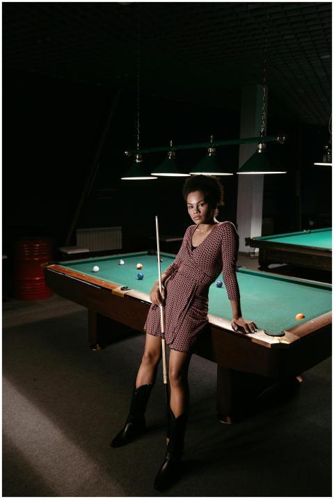 Confident woman holding cue stick by a billiard ta