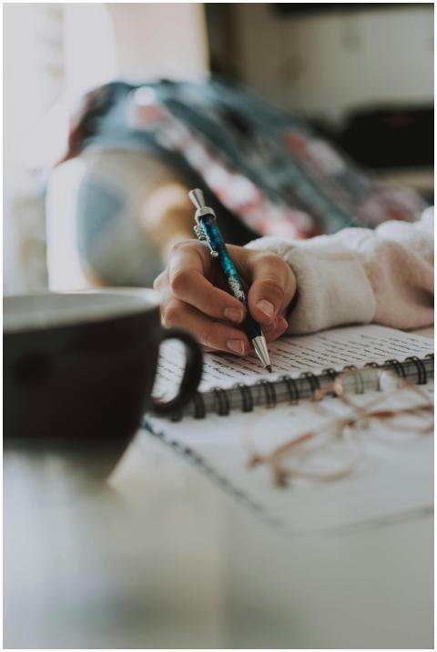 A person writes in a notebook while a cup of coffe