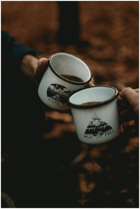 Two people toasting with enamel mugs around a camp
