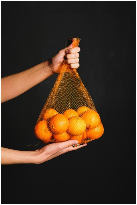 A hand holding a net bag full of fresh oranges aga