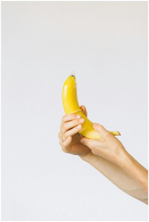 A banana held in hands with a condom on top symbol