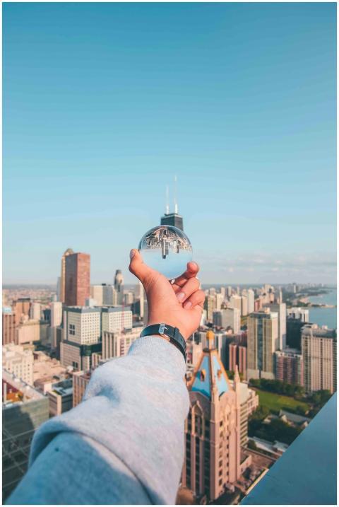 A hand holds a glass sphere reflecting a city's sk