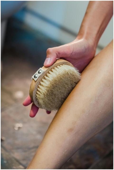 Hand using a body brush on leg for personal hygien