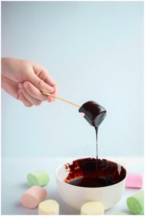 A hand dipping a marshmallow into a bowl of rich c