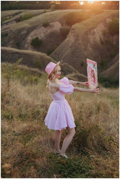 Elegant woman in pink dress and hat showcasing art