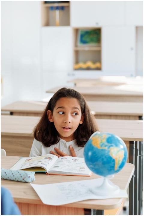 A young girl in a classroom studies a globe, learn