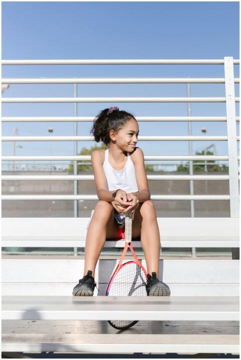 Young girl sitting on bleachers with tennis racket