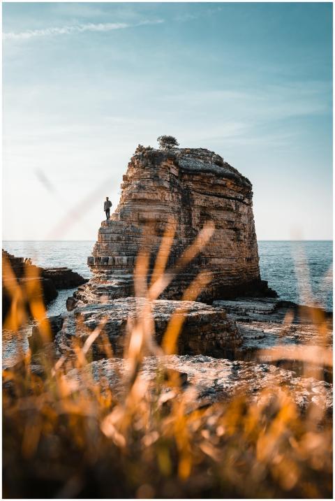 Lone person standing on a towering coastal rock wi