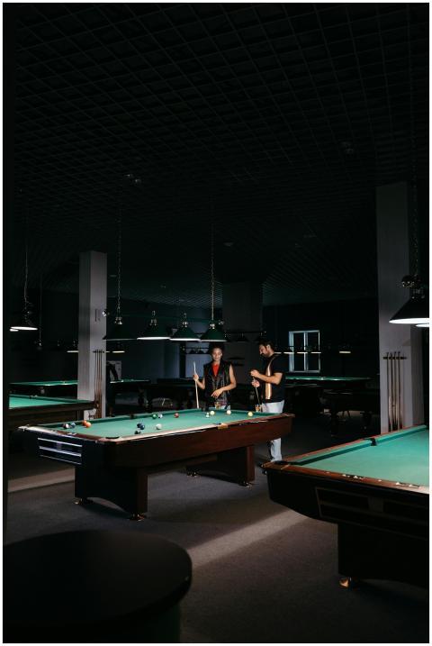 Two adults playing billiards on a dimly lit table,
