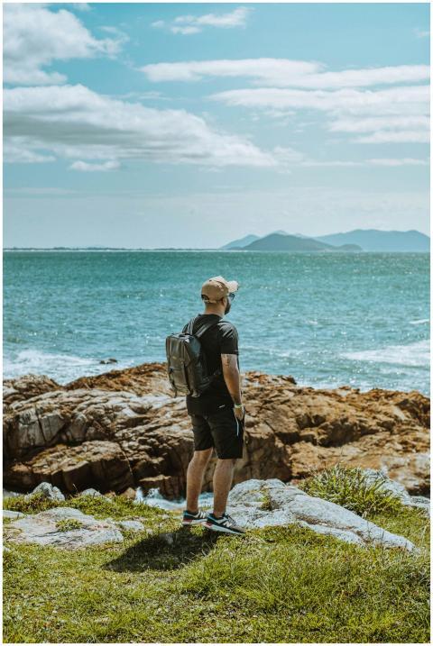 A man stands on a rocky cliff, gazing at the ocean