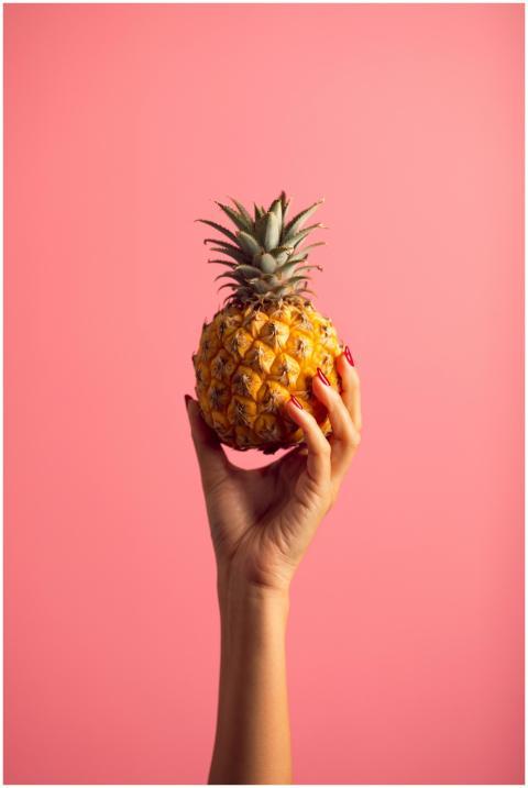 A hand with polished nails holds a ripe pineapple