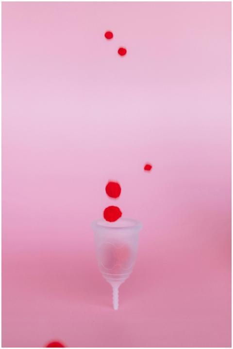 A menstrual cup set against a pink background with