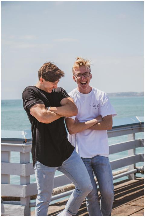 Two men laughing and posing outdoors against a sea