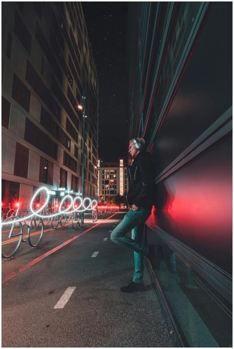 A man in Oslo leans against a wall with light trai
