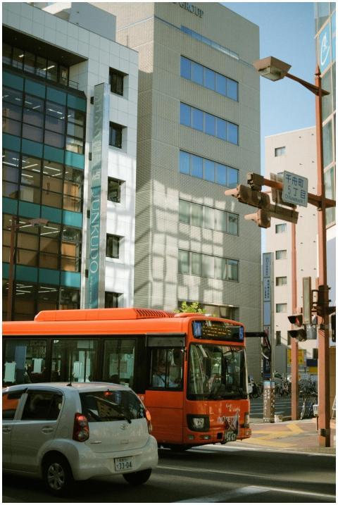A vibrant orange bus and car on a bustling city st