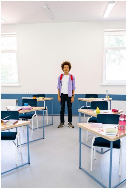Teenager standing in a well-lit classroom with tab