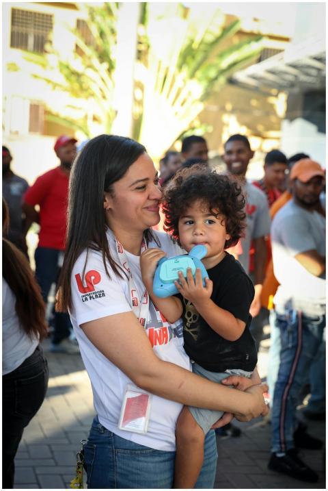 A smiling mother holds her young child at a lively