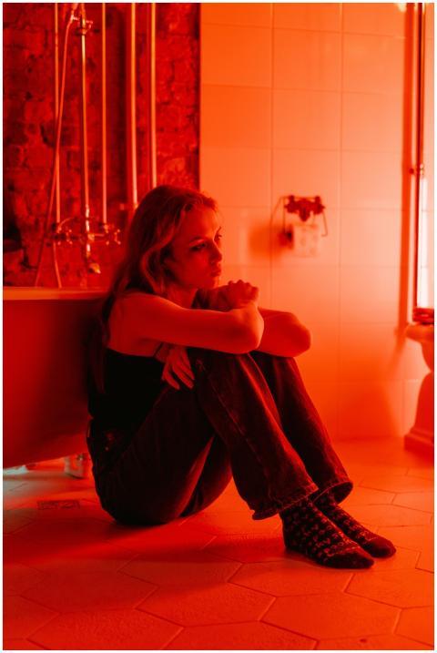 A woman sits thoughtfully in a dimly lit red bathr
