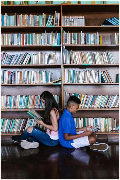 Two children sitting back to back reading books in