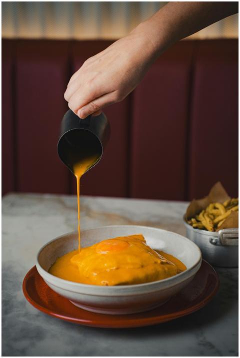 Hand pouring cheese sauce over a dish in a casual