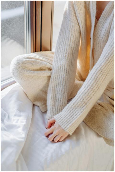 Woman in a cozy sweater sits by a sunlit window, e