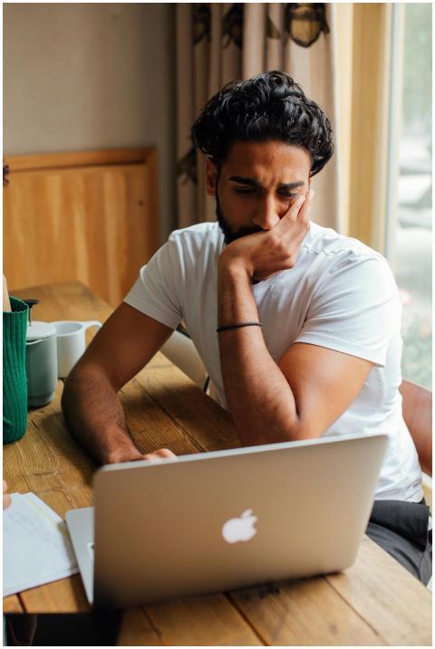 Man in white shirt pondering work on laptop at a c