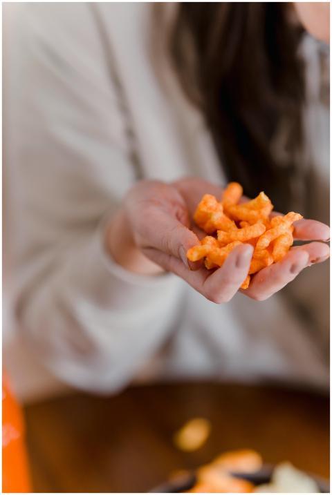 Person holding orange crunchy snack in hand, blurr