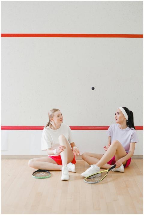 Two women sitting on the squash court with rackets