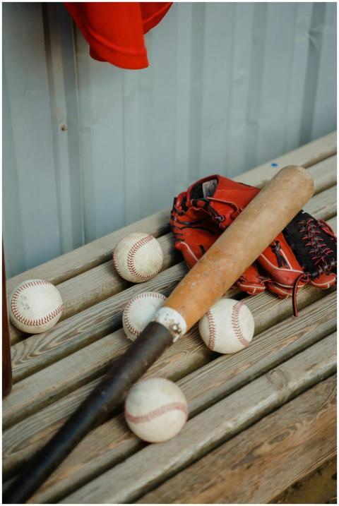 A baseball bat, balls, and a glove on a wooden ben