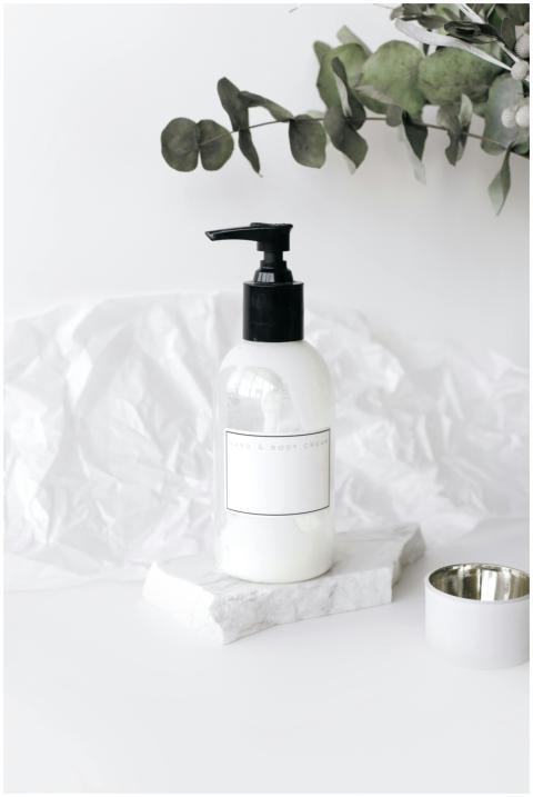 Elegant lotion bottle on marble with green leaves,