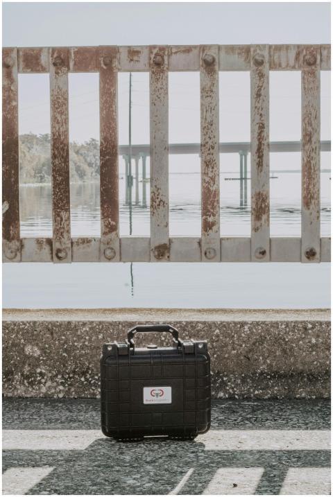 A black hard-shell suitcase placed near a rusty br