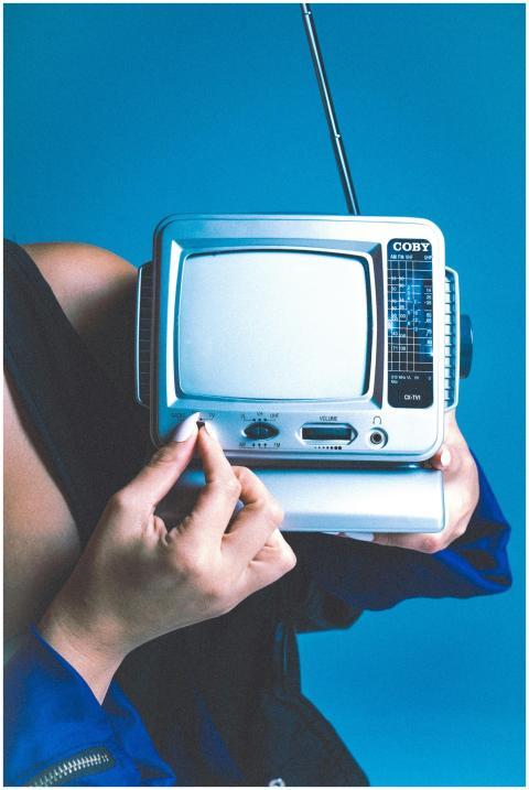 A woman holds a retro portable TV against a vibran