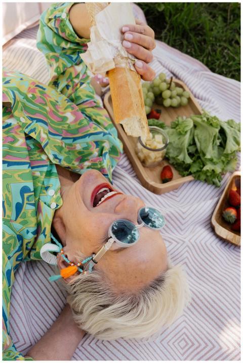 Senior woman lying on grass at picnic, eating bagu