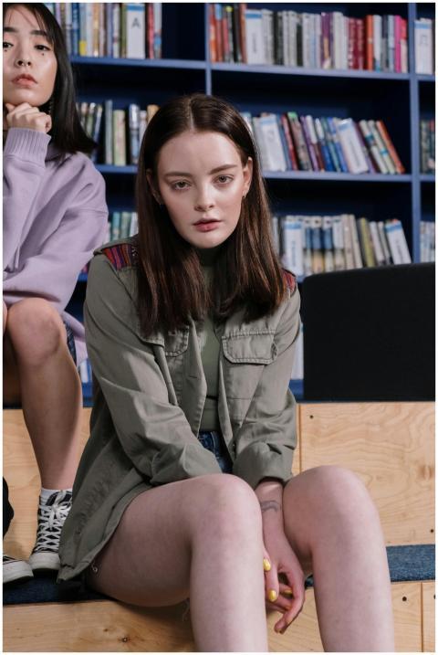 Two teenage girls sitting in a modern library, wea