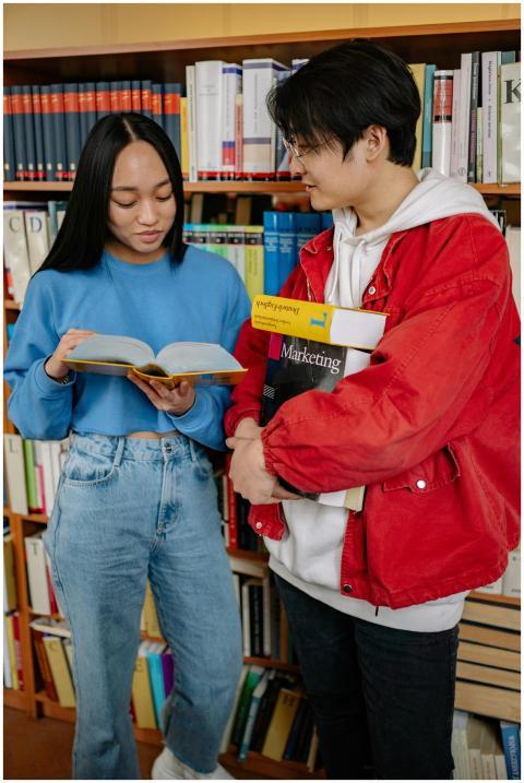Two students discussing a book in a library, foste