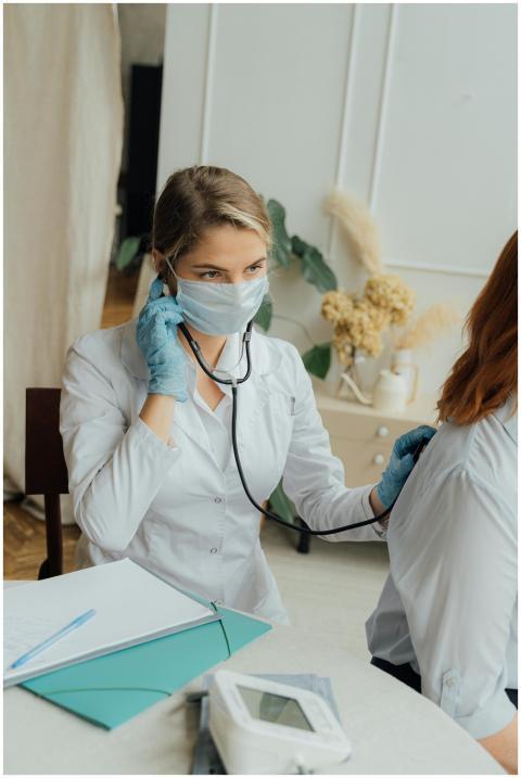 A healthcare professional in PPE using a stethosco
