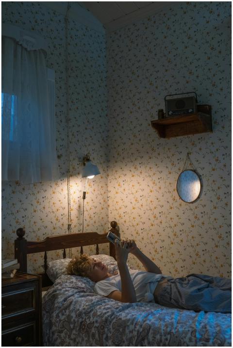 A teenager lies on a bed using a smartphone in a c