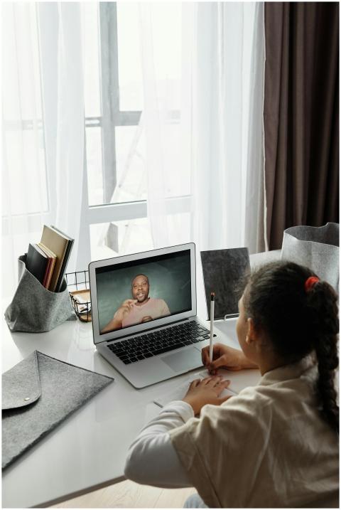 A young girl takes notes during an online class wh