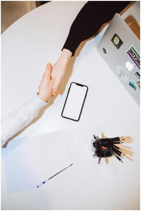 Two individuals shaking hands across a desk with a