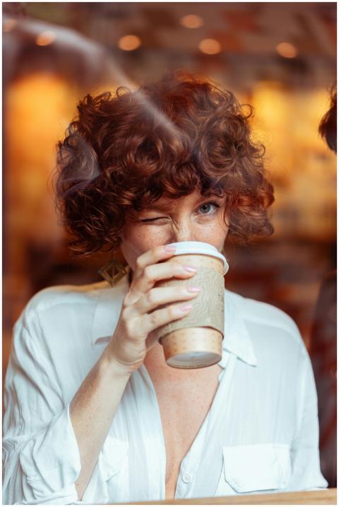 Curly-haired woman sipping coffee through a cafe w