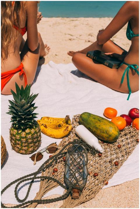 Two women enjoying a sunlit beach picnic with trop