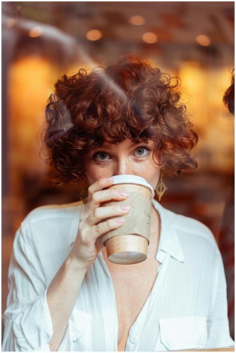A woman with curly red hair savoring a coffee indo